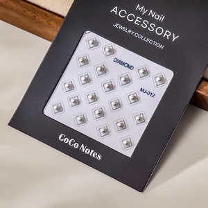 Macro detail of square pearl nail art studs with silver metal frames in black packaging