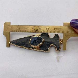 Macro shot measuring a 65mm black arrowhead pendant with gold trim and blue stone inlay