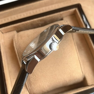Close-up of silver metal watch case with side crown and premium black leather strap