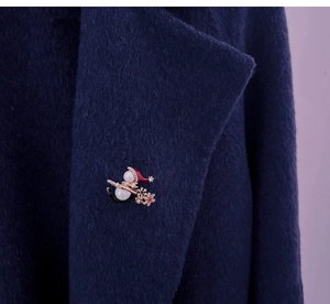 Detailed view of a Christmas snowman brooch with red hat on a navy wool coat lapel