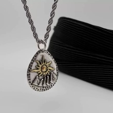 Close-up of a two-tone triangular Evil Eye pendant with sun and mountain motifs