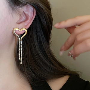 Macro shot of gold heart tassel earrings with crystals worn by a model in warm light