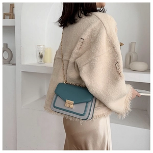 Detail of color-block crossbody bag with gold chain strap and metal clasp on a model