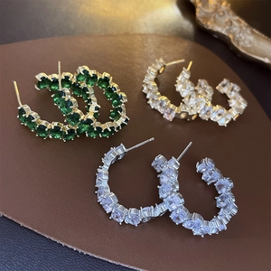 Three pairs of C-shaped hoop earrings with faceted gems on a brown leather surface