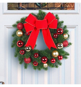 Detail of green Christmas wreath with red bow and gold baubles hanging on a white door