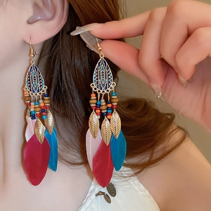 Detail of bohemian drop earrings featuring colorful feathers and golden leaf charms