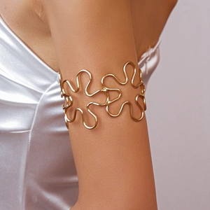 Detailed view of a wavy hollow golden flower arm cuff on a model's upper arm