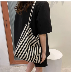 Detail of a large black and white striped canvas tote bag worn by a model in a minimalist room