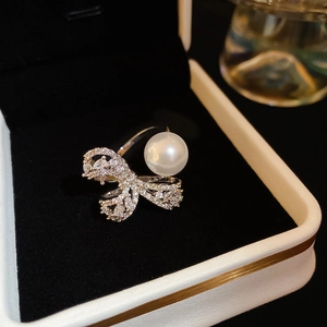 Detailed view of zircon bow ring with large pearl on black velvet display base