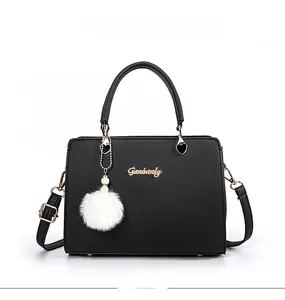 Detail of black leather tote bag with gold logo, white fur ball charm and pearl accents