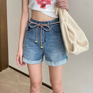 Detail of blue denim shorts with high waist, rolled cuffs and decorative beaded cord belt