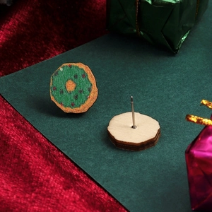 Macro detail of wooden donut earrings with green glaze and silver stud on red velvet