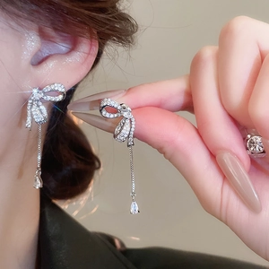 Macro shot of silver bow tassel earrings with sparkling cubic zirconia on model ear