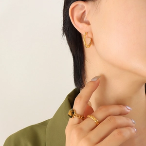 Minimalist gold-plated twisted hoop earrings and gemstone rings worn by a model