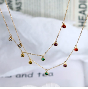 Detail of 18K gold-plated necklaces with colorful round crystal charms on white fabric