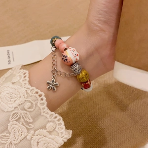 Detailed close-up of ceramic Maneki Neko bead and flower charm on colorful beaded bracelet