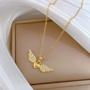 Close-up of golden heart wing pendant with sparkling crystals on white silk