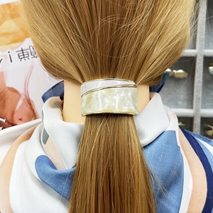 Detail of marble-patterned ponytail cuff with golden metal edges in cream and beige