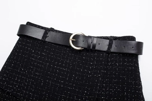 Détail d'une jupe en tweed noir et ceinture en cuir avec boucle dorée en forme de C