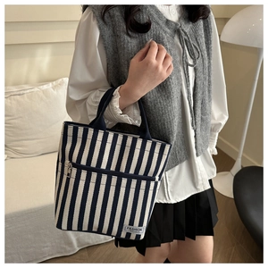 Detail of striped canvas tote bag with front zipper pocket and Fashion Instinct logo