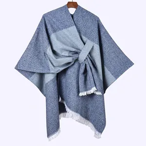 Detail of blue-grey plaid knit poncho featuring fine white fringe and soft fabric texture