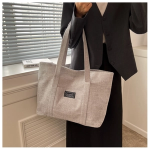 Detail of grey textured fabric tote bag showing outer pocket and black fashion label