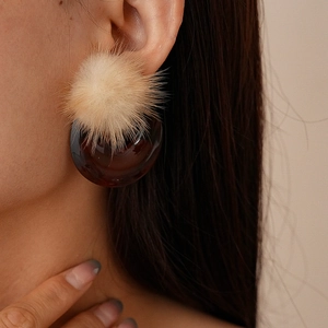 Close-up of retro hollow resin earring with beige pom-pom on model's left ear
