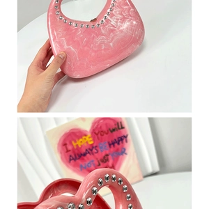 Detail of pink heart-shaped acrylic clutch bag with marble texture and rhinestone handle