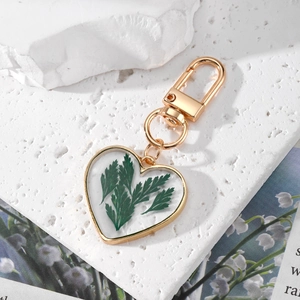Handmade heart resin keychain with real dried flowers and golden metal frame on marble