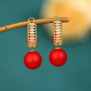 Detail of elegant gold drop earrings with marquise crystals and a matte red pearl drop