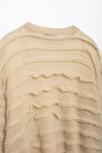 Detail shot of beige knit sweater showing layered wave textures and intricate hollow patterns
