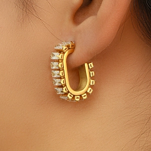 Close-up of gold-plated U-shaped earrings with square zircon stones on a female model
