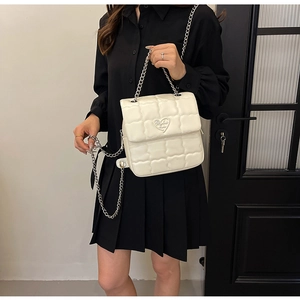 Detail of white quilted crossbody bag with heart logo and silver chain on a black dress