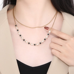 Close-up of a layered gold necklace featuring black and white heart pendants on a model