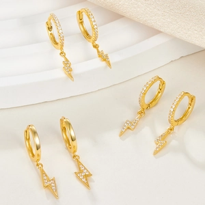 Three gold lightning bolt earrings with pavé zircons on elegant white pedestal