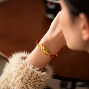 Detail of goldfish charm bracelet with matte gold finish and red woven silk rope
