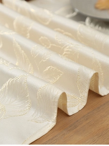 Macro shot of gold leaf embroidery on beige fabric with detailed silk texture and sheen