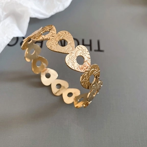 Close-up of golden hollow heart-shaped bracelet with detailed floral pattern engraving