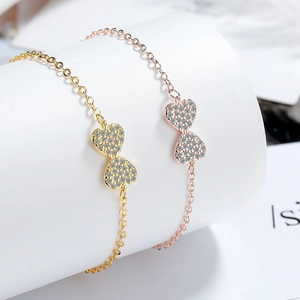 Elegant zircon bowknot bracelet in gold and rose gold finish with sparkling double heart charms