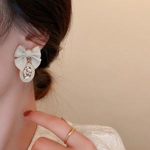 Close-up of a vintage fabric bow earring with an elegant faux pearl dangle on a model