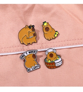 Vue macro de quatre pin's capybara en émail sur tissu rose montrant les détails fins