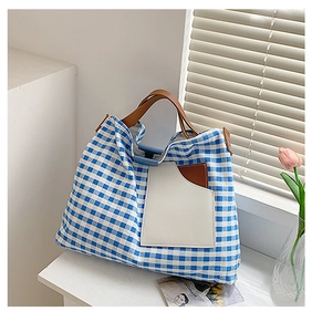 Blue and white checkered canvas tote bag with brown leather handles on a sunlit table