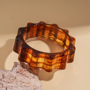 Detailed macro view of the amber resin bangle featuring wavy edges and tortoiseshell texture