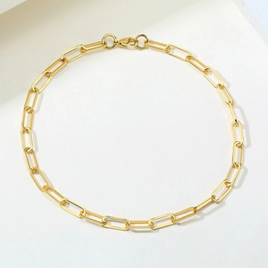 Detail of golden paperclip chain necklace with circular clasp and extender on white surface