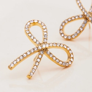 Classic 18K gold stainless steel bow earrings with white crystals on a reflective surface