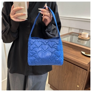 Détail d'un sac à main bleu vif matelassé avec surpiqûres en cœur et poignée en tissu