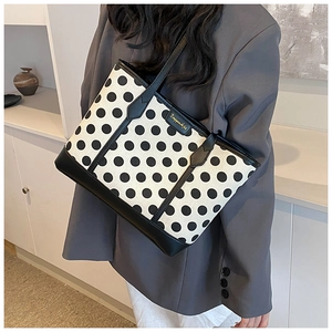 Close-up of a white tote bag with black polka dots and gold logo on a grey blazer