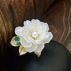 Macro detail of camellia brooch with white petals, gold leaves, and centered pearl