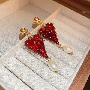 Boucles d'oreilles cœur vintage avec perles baroques et émail rouge sur fond beige