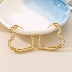Golden heart hoop earrings with CNC cubic zirconia stones on a ceramic background